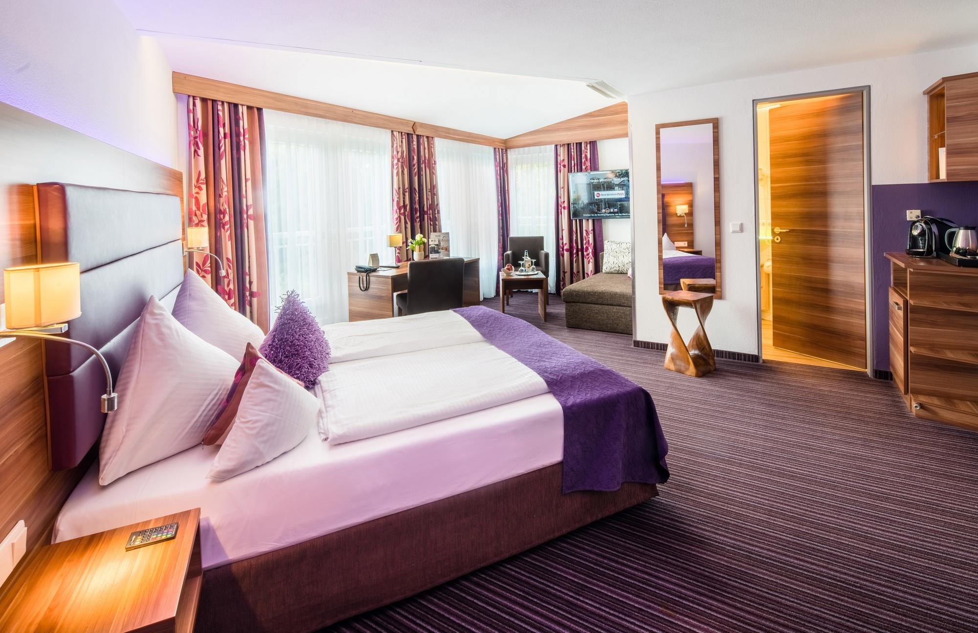 Stilvoll eingerichtetes Hotelzimmer mit großem Bett, Sitzecke, Schreibtisch, TV und Zugang zum Bad.