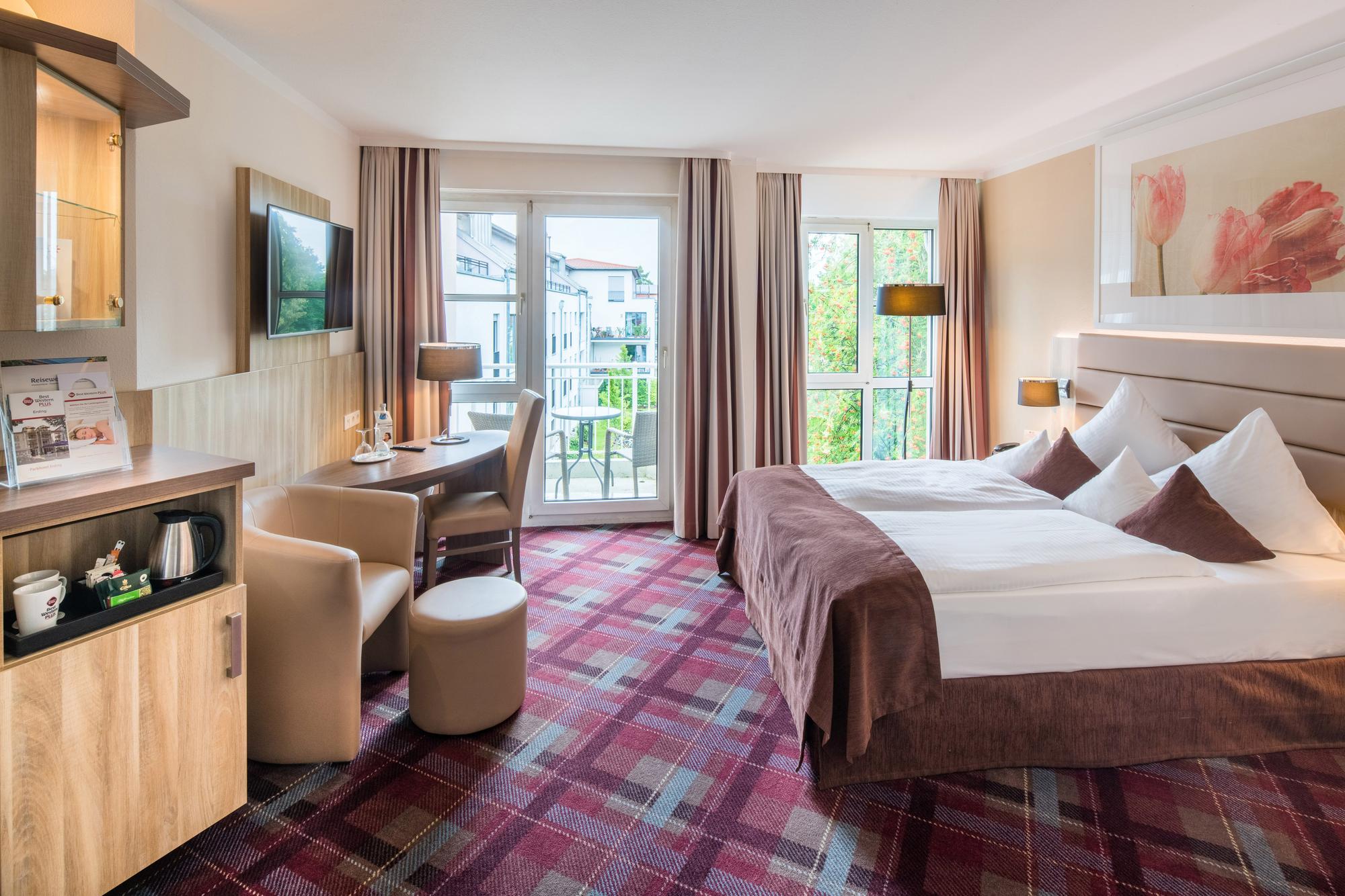Elegantes Hotelzimmer mit Doppelbett, Schreibtisch, Sessel am Fenster, TV und moderner Einrichtung.
