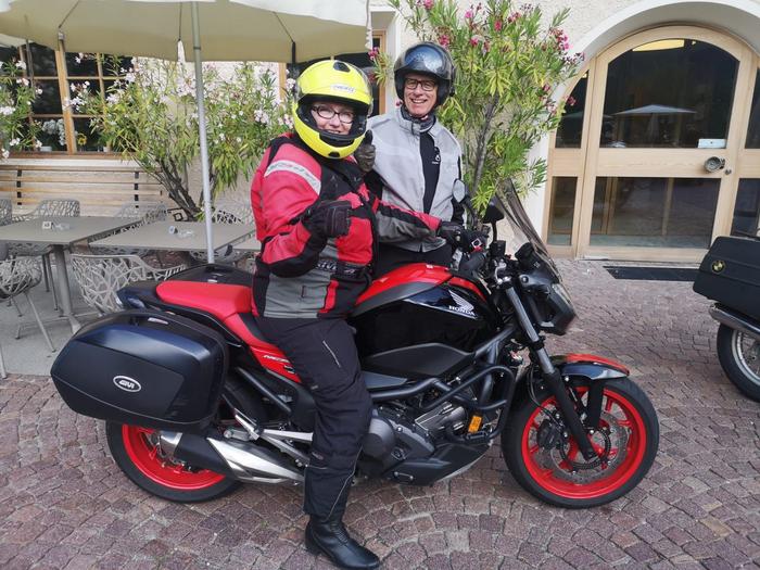 ein Mann und eine Frau mit Helmen auf dem Kopf auf Motorrädern von einem Hoteleingang parkend.