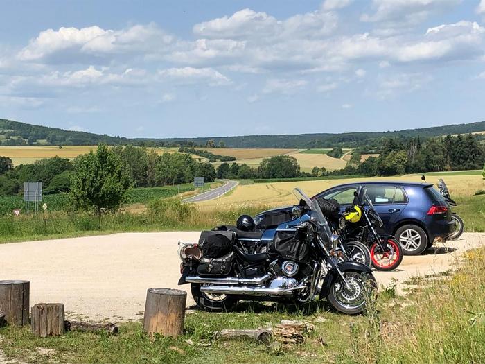 Ländliche Straße mit zwei Motorrädern am Straßenrand geparkt, umgeben von Feldern und Hügeln