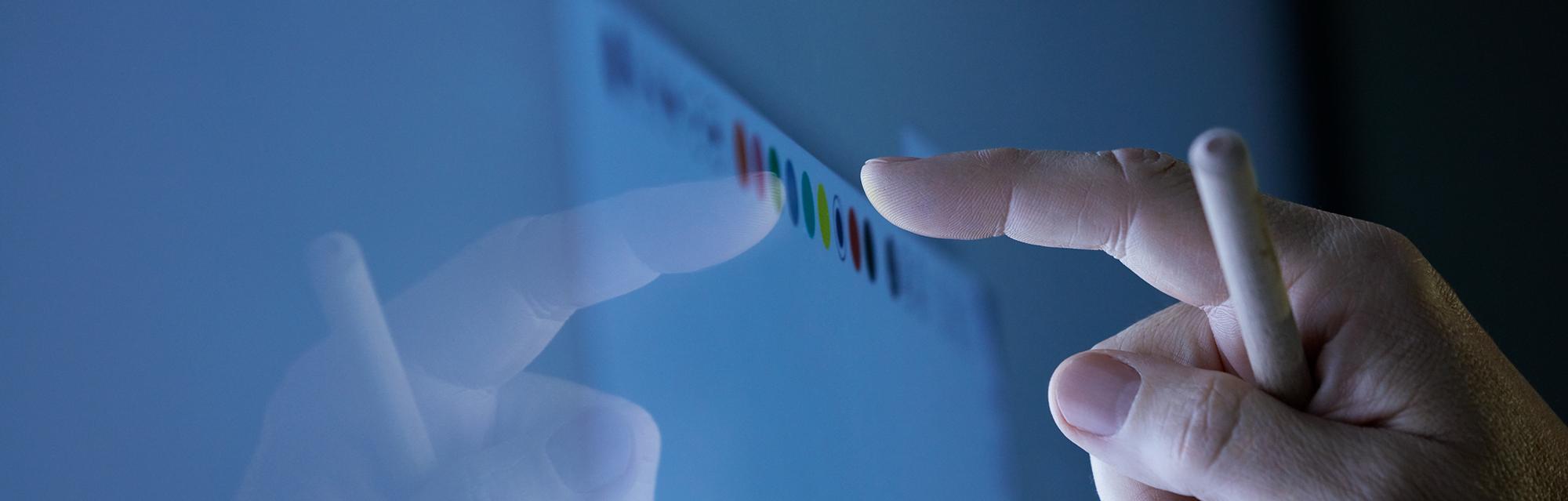 Nahaufnahme einer Hand, die mit Finger und Stift farbige Punkte auf einem Touchscreen berührt