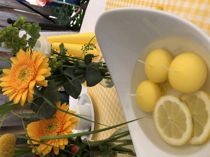 Schale mit Zitronenscheiben in Flüssigkeit, im Hintergrund Vase mit orange-gelben Blumen.