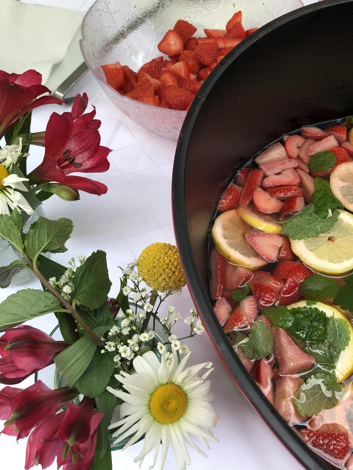 schwarze Schale mit Zitronenscheiben und Erdbeeren auf einer weißen Tischdecke zusammen mit einer Blumenvase.